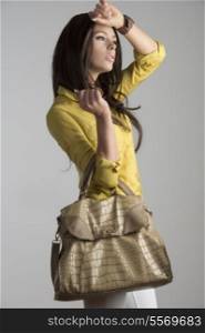 sexy brunette girl in fashion pose taking big vogue bag in the hand and wearing yellow skirt and white pants.