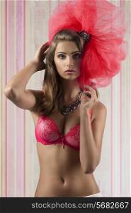 sexy brunette woman posing with red bra and big tulle accessory on the head, looking in camera