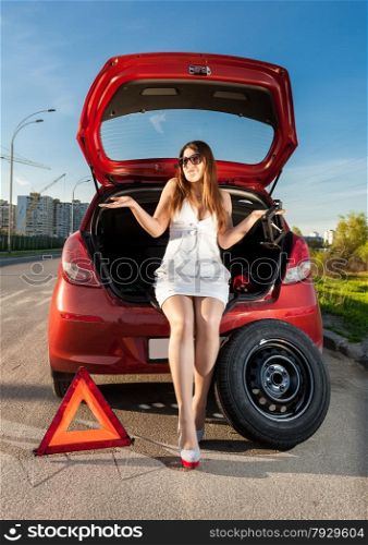 Sexy brunette woman sitting in trunk of broken car
