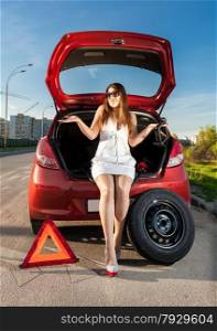 Sexy brunette woman sitting in trunk of broken car