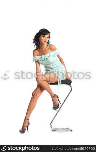 Sexy brunette woman wearing short dress isolated sit on stool on white background. Full body portrait. Happy woman in dress on a chair