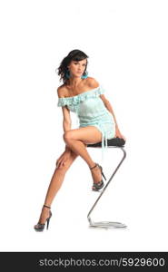 Sexy brunette woman wearing short dress isolated sit on stool on white background. Full body portrait. Happy woman in dress on a chair