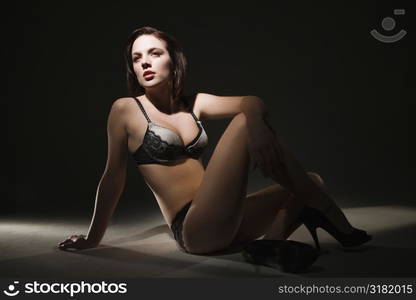 Sexy Caucasian woman in lingerie and heels sitting on floor.