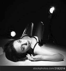 Sexy Caucasian woman in lingerie lying on floor with spotlights looking up at viewer.