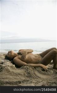 Sexy Caucasian young adult nude woman lying on beach.