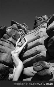 Sexy Caucasian young adult woman standing nude against rocks in Maui with back arched and arms stretched over head.
