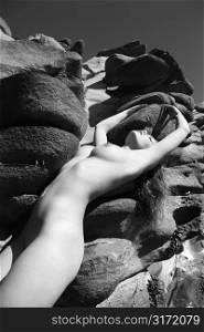 Sexy Caucasian young adult woman with eyes closed standing nude against rocks at Maui coast with arms stretched over head.