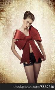 sexy christmas portrait of beautiful young female posing with elegant hair-style, colorful make-up and big red bow on her naked breast, adorned like a gift.