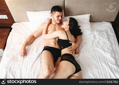 Sexy couple lying and kissing on big white bed. Love games in bedroom, hot sex lovers. Sexy couple lying and kissing on big white bed