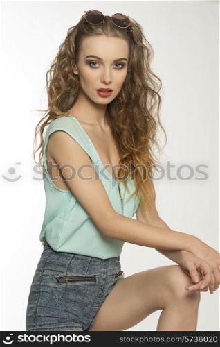 sexy curly woman with long hair, stylish make-up, sexy denim shorts, blue shirt and vintage sunglasses on the head . In sensual pose looking in camera