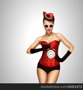 Sexy dream.. Sexy pinup girl in a red vintage corset holding a retro alarm clock on grey background.