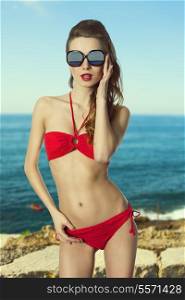 sexy fit female in holiday time posing with red swimwear, sunglasses and natural hair-style.
