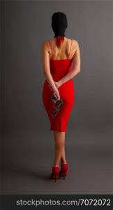 sexy girl in a tight red dress and balaclava holds an automatic pistol on her back against a dark background