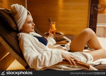 Sexy girl in bathrobe and towel on the head relaxing with cocktail in spa chair. Relaxation leisure, healthy lifestyle, attractive woman resting in armchair, beauty salon. Sexy girl relaxing with cocktail in spa chair