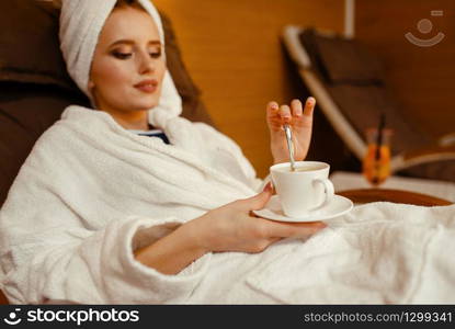 Sexy girl in bathrobe and towel on the head relaxing with cup of coffee in spa chair. Relaxation leisure, healthy lifestyle, attractive woman resting in armchair, beauty salon. Sexy girl relaxing with cup of coffee in spa chair