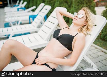 Sexy girl in swimsuit sunbathing on the deck chair. Slim woman relax near the swimming pool. Summer vacations