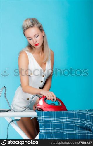 Sexy girl retro style ironing male shirt, woman housewife in domestic role. Traditional sharing household chores. Pin up housework. Vivid blue background