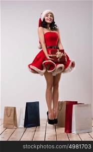 Sexy girl wearing Santa Claus clothes - dress and hat jumping with Christmas gifts. Full length portrait