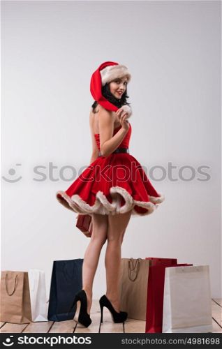 Sexy girl wearing Santa Claus clothes - dress and hat standing with Christmas gifts. Full length portrait