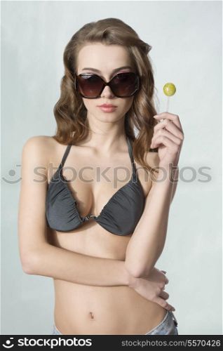 sexy girl with bikini, sunglasses and long hair posing with lollipop in summer portrait