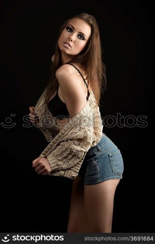 sexy girl with open sweater and shorts jeans, her body is turned in profile with nacked left shoulder and looks in to the lens