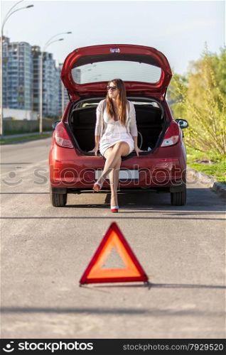 Sexy helpless woman sitting near broken red car