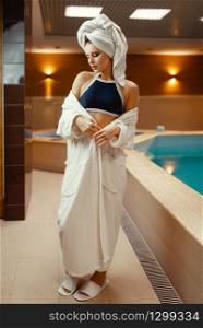 Sexy lady in towel on the head and body at the pool side indoors. Swimming and relaxation, healthy lifestyle, attractive woman in spa salon