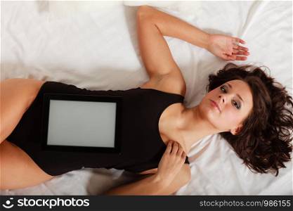 Sexy lazy girl in body underwear lying with tablet touchpad blank copy space on bed. Woman relaxing lazing in bedroom. Internet.