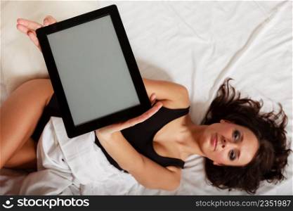 Sexy lazy girl in body underwear showing copy space on tablet touchpad on bed. Woman relaxing lazing in bedroom. Technology.
