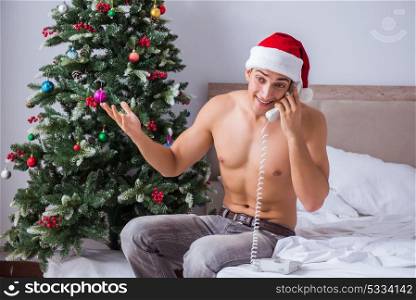Sexy man in the bed wearing santa hat in christmas concept