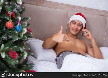 Sexy man in the bed wearing santa hat in christmas concept