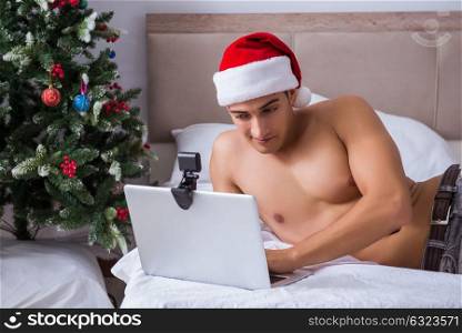 Sexy man in the bed wearing santa hat in christmas concept. The sexy man in the bed wearing santa hat in christmas concept