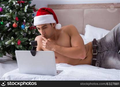 Sexy man in the bed wearing santa hat in christmas concept. The sexy man in the bed wearing santa hat in christmas concept
