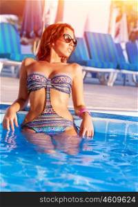 Sexy model wearing stylish colorful swimwear relaxed in poolside, luxury beach hotel, enjoying refreshing cold water in hot summer day, vacation concept