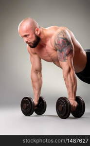 Sexy muscular bodybuider doing push ups with weights on the gray background