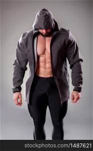 Sexy muscular bodybuider posing with sweatshirt and hood on the gray background