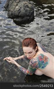 Sexy nude Caucasian tattooed woman lying in tidal pool in Maui, Hawaii, USA.