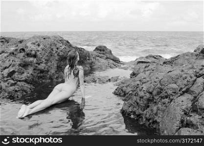 Sexy nude Caucasian woman doing yoga pose in tidal pool on beach in Maui, Hawaii.