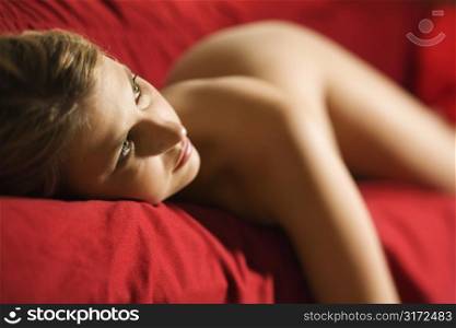 Sexy nude Caucasian young adult female lying seductively on red couch looking at viewer.