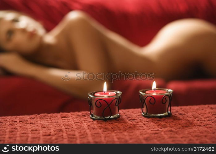 Sexy nude Caucasian young adult female lying seductively on red couch with candles.
