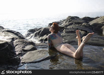 Sexy nude tattooed Caucasian woman lying in tidal pool in Maui, Hawaii, USA.