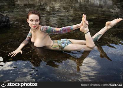 Sexy nude tattooed Caucasian woman lying in tidal pool in Maui, Hawaii, USA.