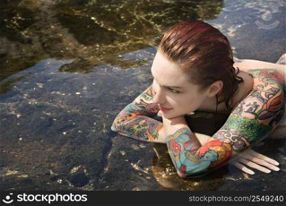 Sexy nude tattooed Caucasian woman lying in tidal pool in Maui, Hawaii, USA.