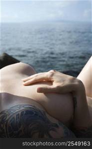 Sexy nude tattooed Caucasian woman lying on rocks overlooking Pacific Ocean in Maui, Hawaii, USA.