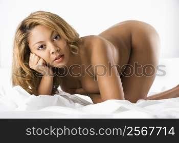Sexy nude woman kneeling on bed making eye contact.