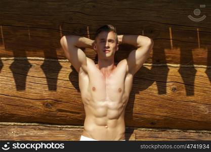 Sexy portrait of a very muscular shirtless male model in the shadow on the background of the old wooden walls
