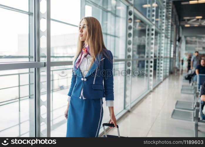 Sexy stewardess with suitcase in airport waiting room. Air hostess in suit with luggage, flight attendant occupation, aviatransportations job. Stewardess with suitcase in airport waiting room