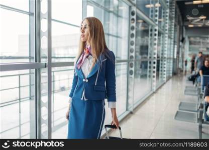 Sexy stewardess with suitcase in airport waiting room. Air hostess in suit with luggage, flight attendant occupation, aviatransportations job. Stewardess with suitcase in airport waiting room