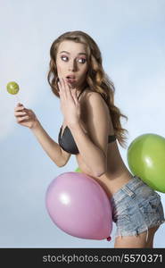 sexy summer posing in funny summer shot with colorful balloons. Posing with long hair, bikini and shorts, eating lollipop