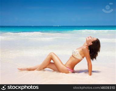 Sexy tanned female lying down on the beach, beautiful slim model posing on seashore, enjoying day spa, luxury tropical resort, summer vacation concept
